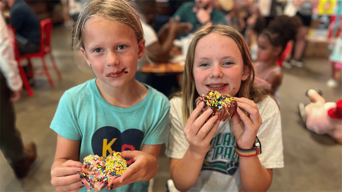 Two sisters smiling with their donuts they decorated at Family Night