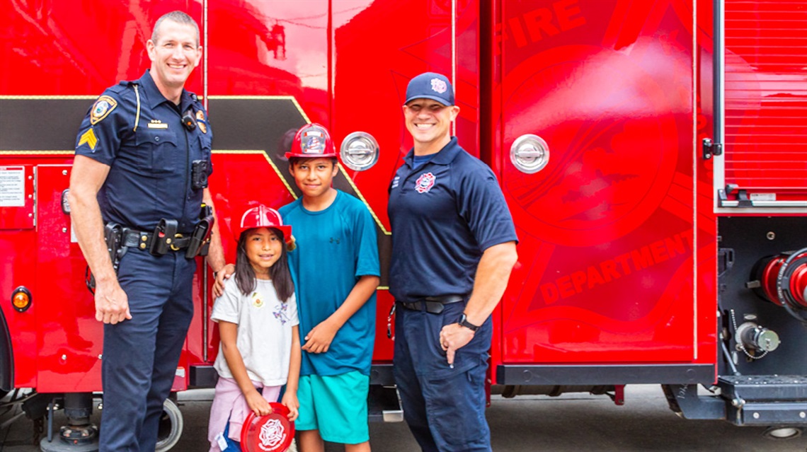 Lenexa police officer and firefighter smiling and posing with two kids