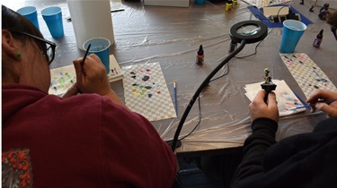 Over the shoulder of woman painting figure on table during Paint-a-Palooza