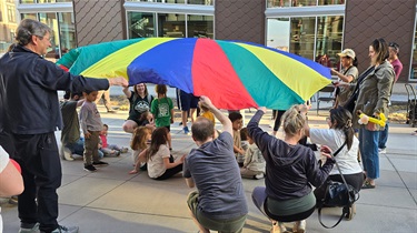 Kids and adults holding onto colorful parachute during storytime at Family Night