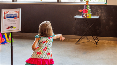 Young girl throwing a bean bag at cans for the Great Market Carnival at the Public Market