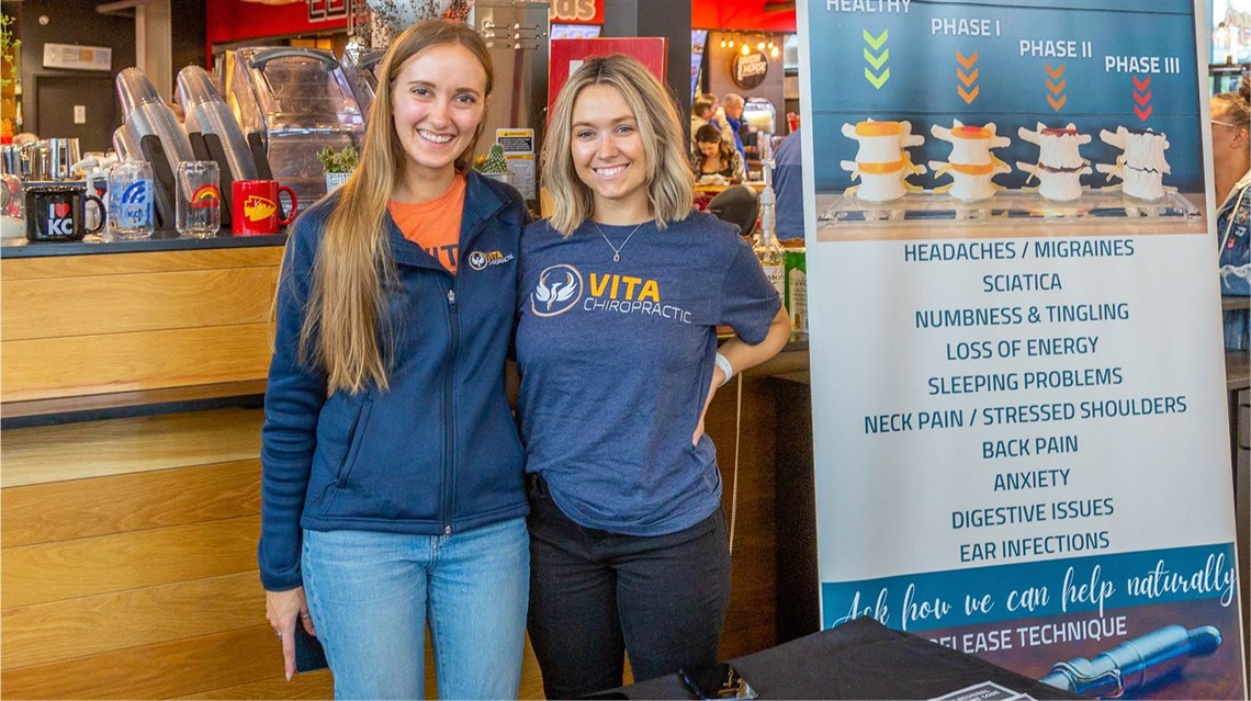 Two co-workers standing in front of sponsor booth inside the Public Market