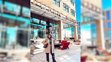 Valerie Bragdon smiling and posing with coffee in hand outside the Lenexa Public Market.