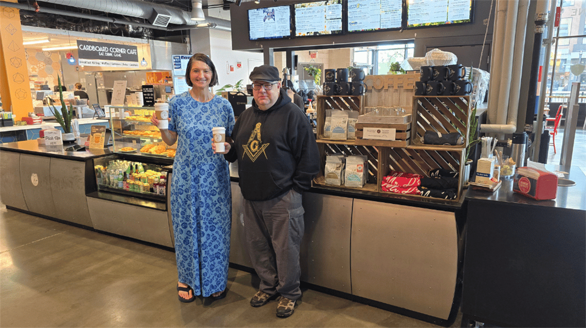 Katy and Ric smiling with coffee in hand in front of Mr. D' Coffee