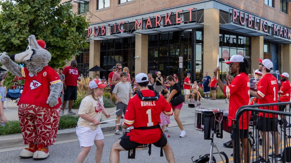 Crowd of people outside the Public Market wathcing the Chiefs Rumble drumline perform and KC Wolf mascot is in the street