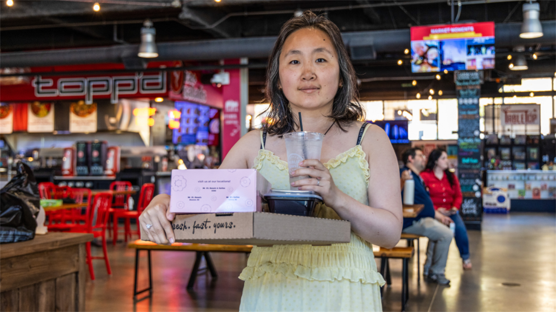 Woman holding a pizza box, donut box, plastic container and water from Public Market merchants.