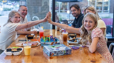 Multigenerational family playing board game at table. Grandmother high fives smiling pre-teen
