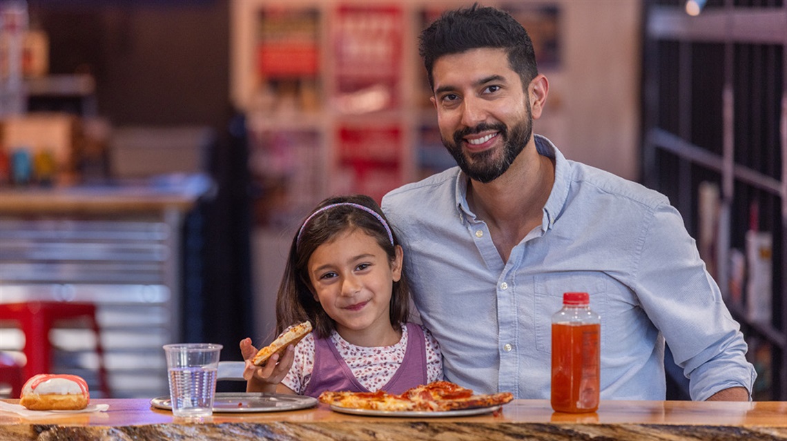 Father and daughter eating pizza and smiling at the Public Market